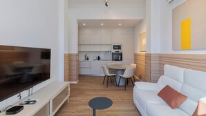 A modern living room with a flat-screen TV, a white sofa, a coffee table, and a dining area with a table and chairs.