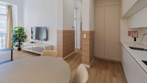 A modern apartment with a dining area, a TV, a plant, and a kitchen.