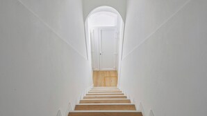A narrow, white-walled stairway with wooden steps leading to a door at the top.