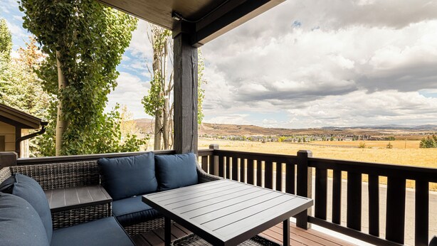 Een overdekt terras met een tafel en kussens, met uitzicht op een prachtig landschap.
