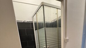 A compact bathroom with a glass shower enclosure, a toilet, and a black tiled wall. - Nuitéa Résidence  (Marseille)