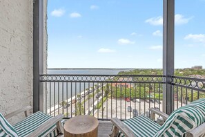 A balcony with a view of a body of water, a parking lot, and buildings in the distance.