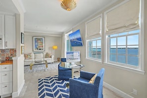 Un salon avec vue sur la mer, un bureau avec un ordinateur et un fauteuil bleu.