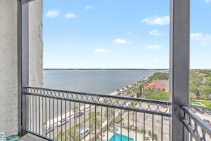 A balcony with a view of a body of water, a street, and residential buildings.
