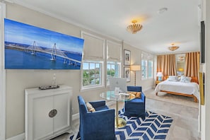 A hotel room with a bed, a desk with a computer, a TV on the wall, and a large window with curtains.