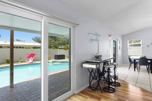 A modern kitchen with a glass door leading to a pool area, a dining table with chairs, and a bicycle. - ⭐ Heated pool near IMG, putting green + arcade (Bradenton)