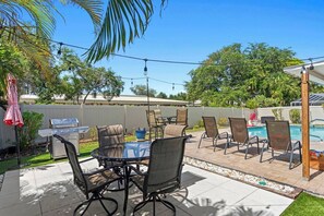 A backyard patio with a grill, outdoor table, chairs, and a swimming pool.