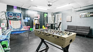 Ein Raum mit einem Kicker, einer Basketball-Spielmaschine und einem grauen Sofa.