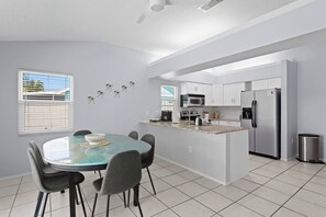 A modern kitchen with white cabinets, a stainless steel refrigerator, and a dining area with a glass table and chairs. - ⭐ Heated pool, Putting Green + Arcade Near IMG (Bradenton)