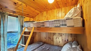 A bunk bed with a ladder, plaid bedding, and a window with checkered curtains. - Hedgehog (Wilson Pond Cabins) (Greenville)