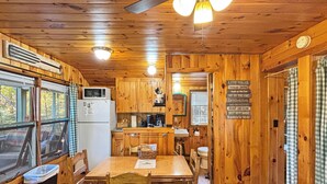 A wooden cabin interior with a dining table, chairs, a refrigerator, a sink, and a sign with activities. - Hedgehog (Wilson Pond Cabins) (Greenville)