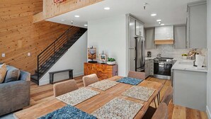A modern kitchen with stainless steel appliances, a dining area with wooden tables and chairs, and a staircase leading to an upper level. - Townhouse w/Lake View #254 at Donner Lake Village (Truckee)