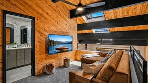 A modern interior with wooden walls, a mounted TV, a sofa, and a dining area. - Townhouse w/Lake View #254 at Donner Lake Village (Truckee)