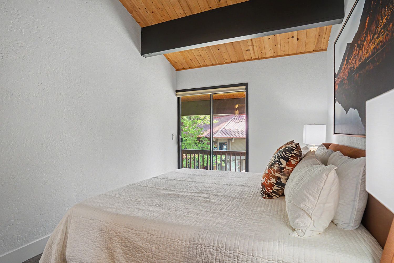 Quarto com uma cama grande, janela com vista para uma casa e teto de madeira.