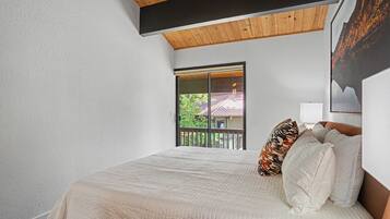 Quarto com uma cama grande, janela com vista para uma casa e teto de madeira.