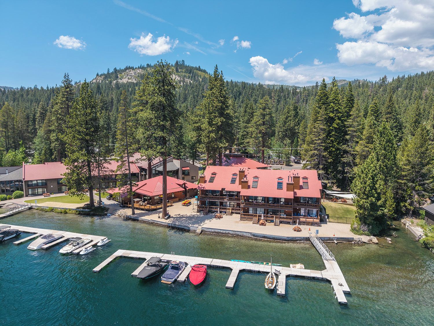 A lakeside lodge with multiple buildings, docked boats, and a forested backdrop.