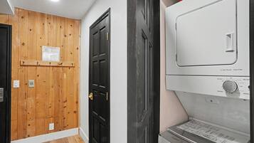 Um corredor com uma porta de madeira, uma porta preta e um eletrodoméstico branco com painel de controle.