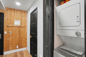Un pasillo con una puerta de madera, una puerta negra y un electrodoméstico blanco con panel de control.