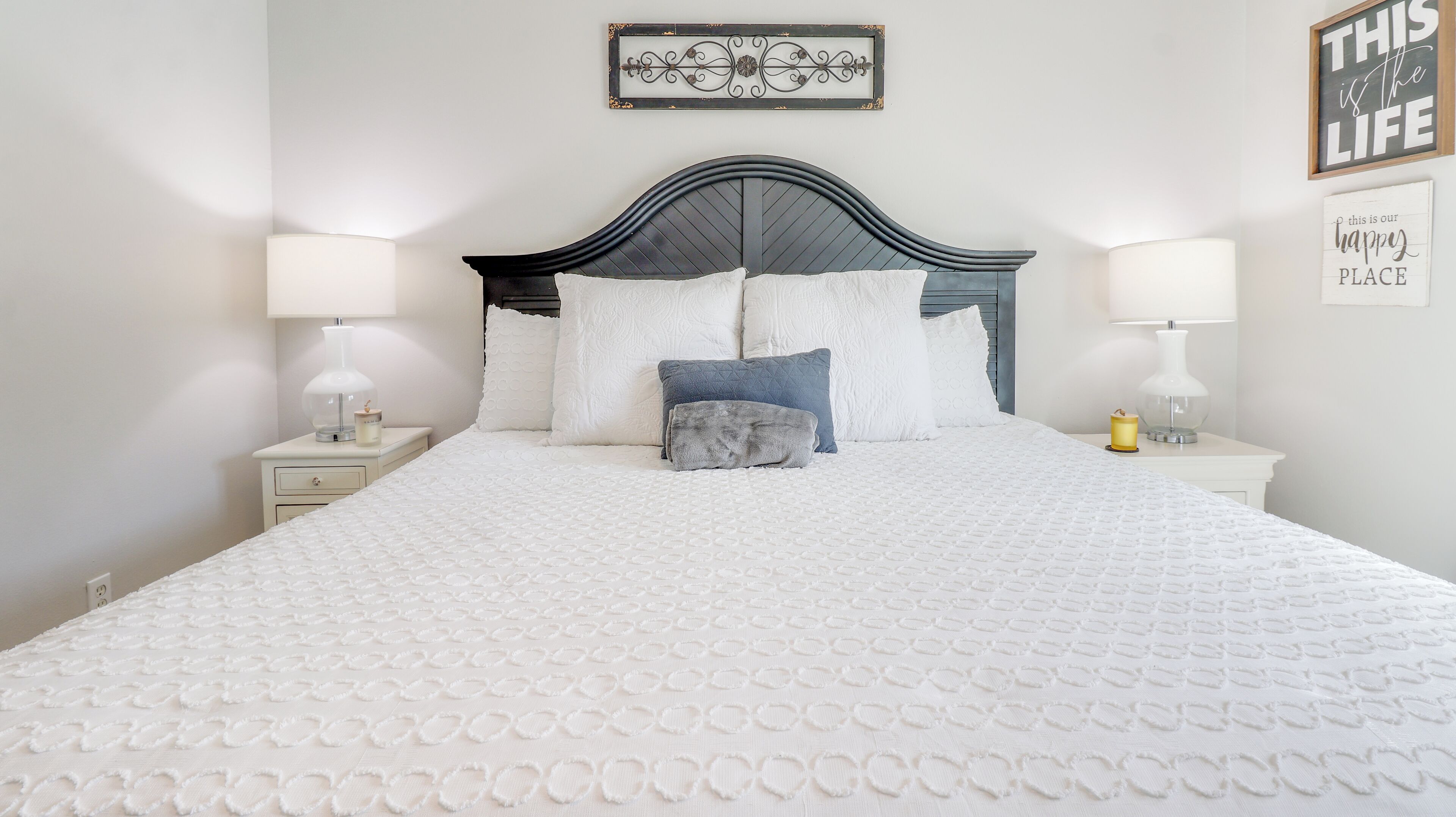 Una cama bien hecha con colcha blanca, dos mesitas de noche con lámparas y decoración mural.