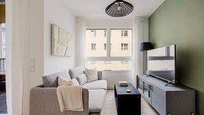 Ett modernt vardagsrum med en grå soffa, ett svart soffbord, en platt-TV placerad på ett grått skåp och en hänglampa.