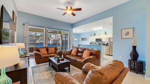 A spacious living room with a brown leather sofa, a coffee table, and a ceiling fan.