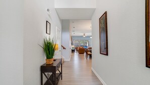 A hallway with a wooden floor, a small table with a plant, and a framed picture on the wall.