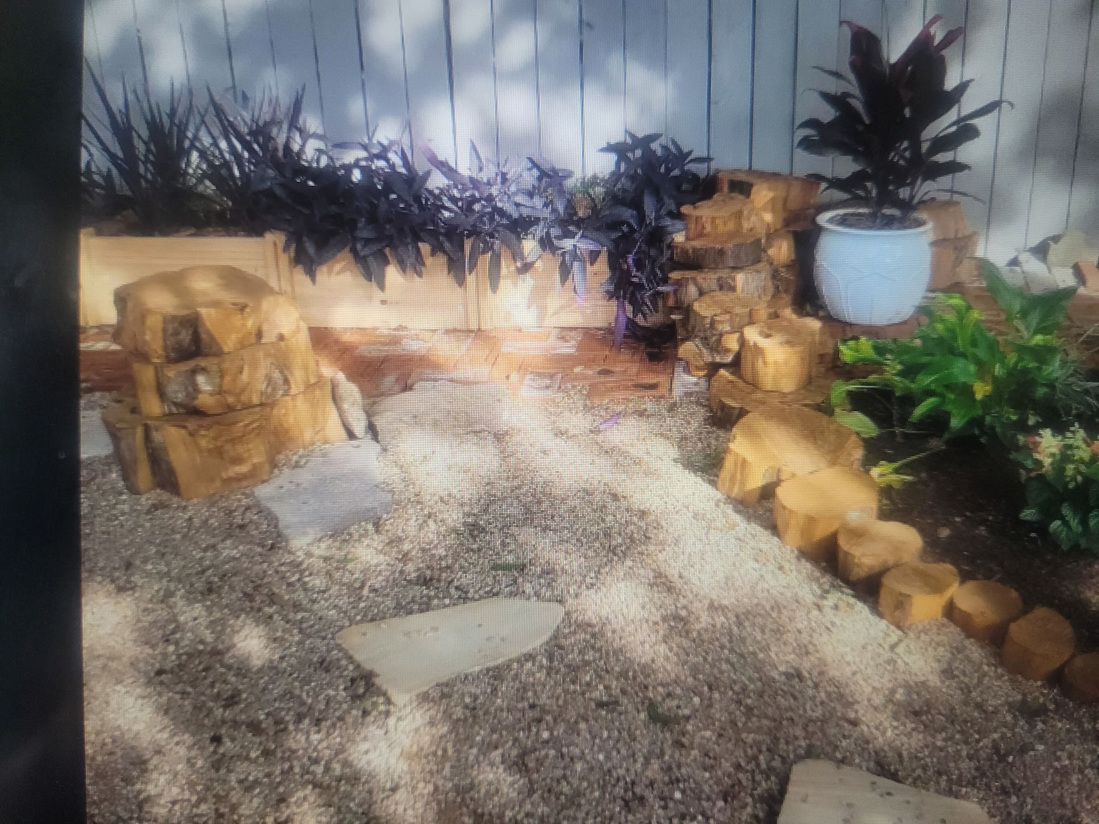 Ein Gartenpfad mit trittfesten Steinen, einem Holzzaun und Kübelpflanzen.