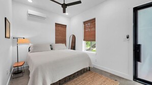 Un dormitorio con cama, lámpara de pie, ventilador de techo y ventana con persianas.