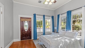 A bedroom with a large bed, a wooden door, and a window with blue curtains. - Charming 3BR Downtown Natchitoches Home, 1.5 Bath, Walking Distance to Front St (Natchitoches)