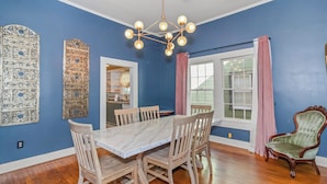 A dining room with a marble table, wooden chairs, a chandelier, and a large window with curtains. - Charming 3BR Downtown Natchitoches Home, 1.5 Bath, Walking Distance to Front St (Natchitoches)