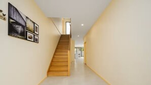Un interno moderno con una scala in legno, pareti chiare e un corridoio che conduce a un'altra stanza.