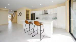 Una cucina moderna con mobili bianchi, un'isola centrale con sgabelli da bar e un frigorifero in acciaio inossidabile.