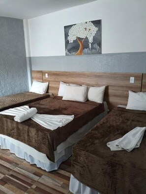 Ein Hotelzimmer mit zwei Betten, jeweils mit brauner Bettdecke und weißen Kissen. Darüber an der Wand hängt ein Baumgemälde.