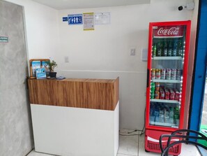 Ein Empfangsbereich mit einem Holzbüro, einem mit Getränken gefüllten Coca-Cola-Kühlschrank und einer blauen Tür im Hintergrund.