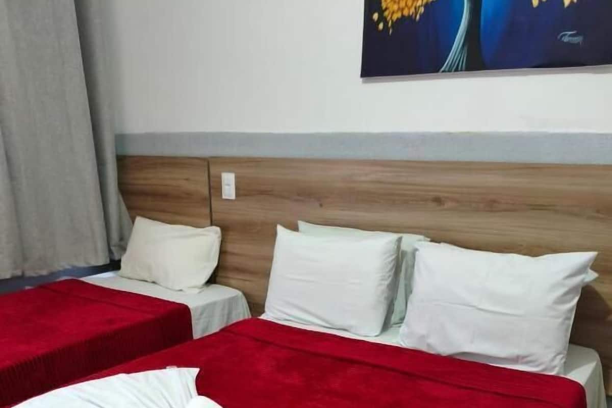 Une chambre d’hôtel avec deux lits, chacun recouvert d’une courtepointe rouge et blanche, agrémentée d’oreillers blancs et d’une serviette blanche soigneusement pliée posée sur le lit.