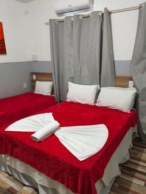 Ein Hotelzimmer mit zwei Betten, grauen Vorhängen und einer roten Bettdecke.