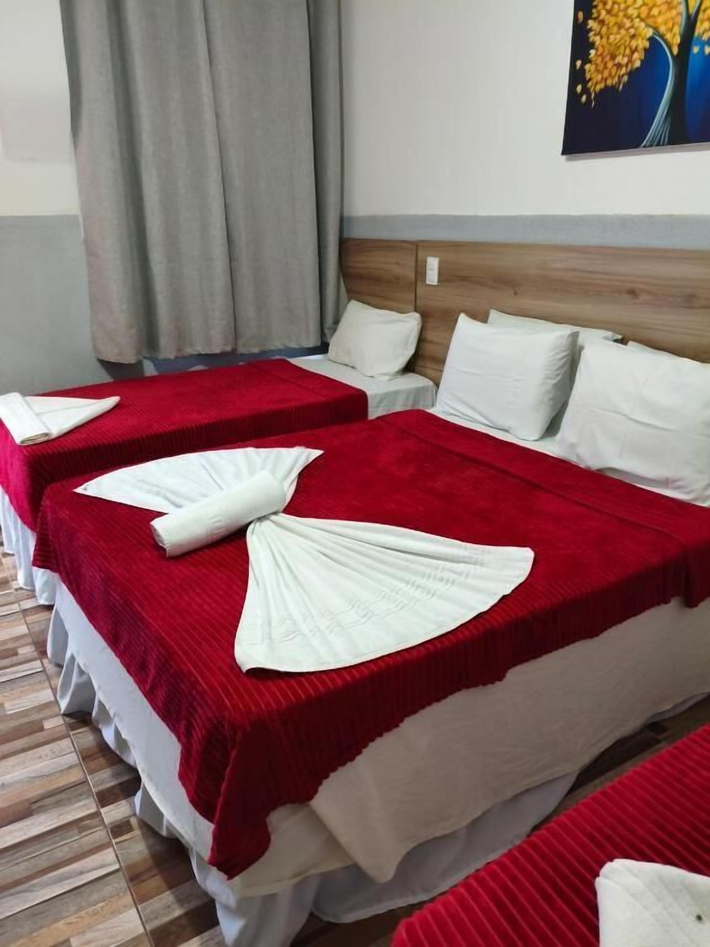 Ein Hotelzimmer mit zwei Betten, jeweils mit einer rot-weißen Decke, weißen Kissen und einem ordentlich gefalteten weißen Handtuch.