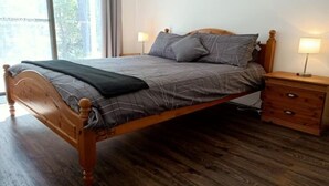 Ein hölzernes Bett mit grau-weißer Bettdecke, zwei Nachttischlampen und ein Nachttisch mit Schubladen.