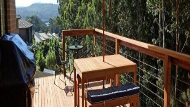Eine Holzterrasse mit Tisch und Stühlen, mit Blick auf ein bewaldetes Gebiet.