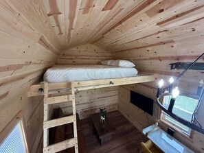 A small, wooden cabin room with a bunk bed, a desk with a lamp, and a window. - Red Tiny Home in Copperhill TN (Copperhill)