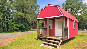 A small red wooden house with a white door, a small porch, and steps leading up to the entrance.