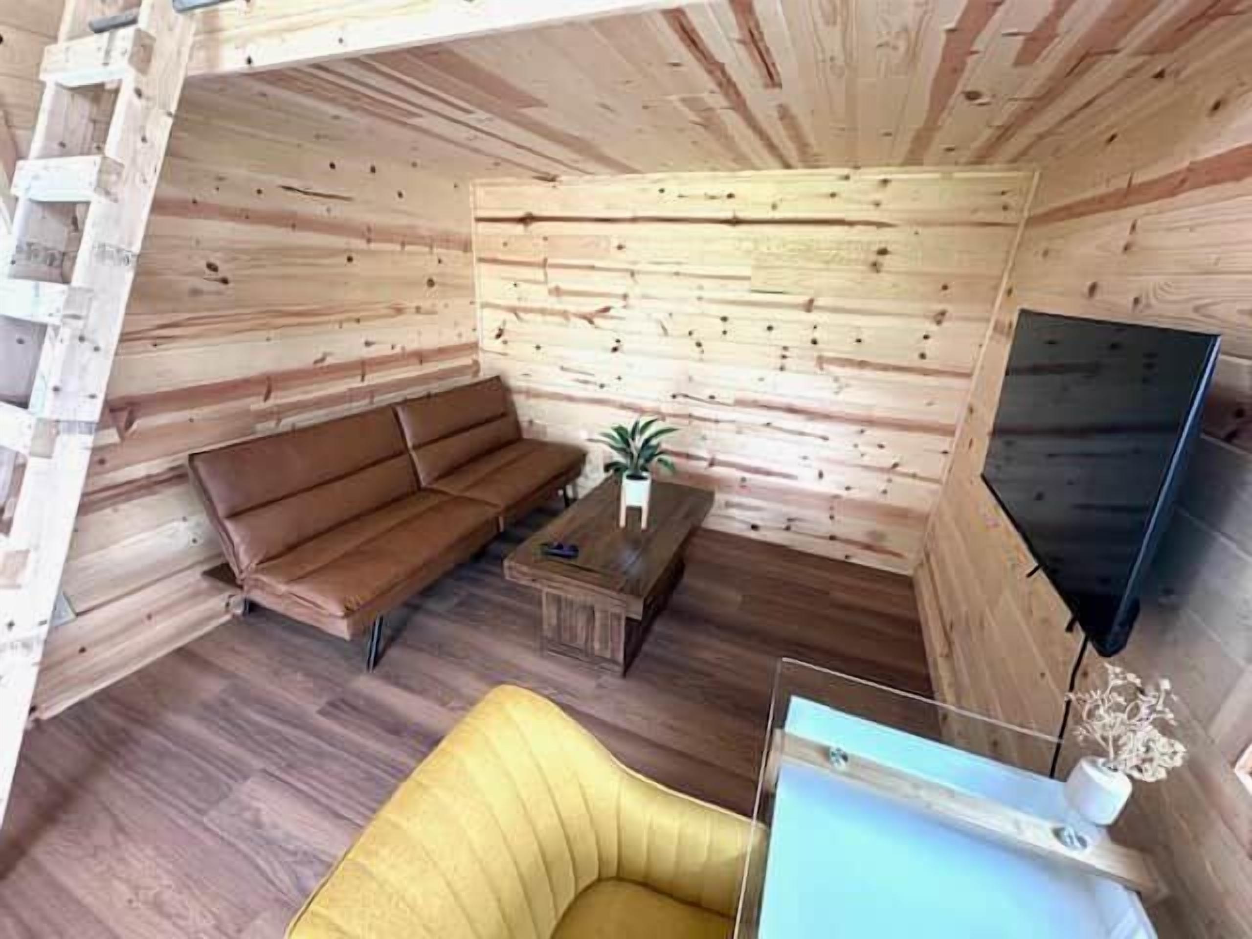 A cabin interior with a sofa, a small table, a TV, and a wooden wall.