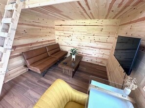A cabin interior with a sofa, a small table, a TV, and a wooden wall. - Red Tiny Home in Copperhill TN (Copperhill)