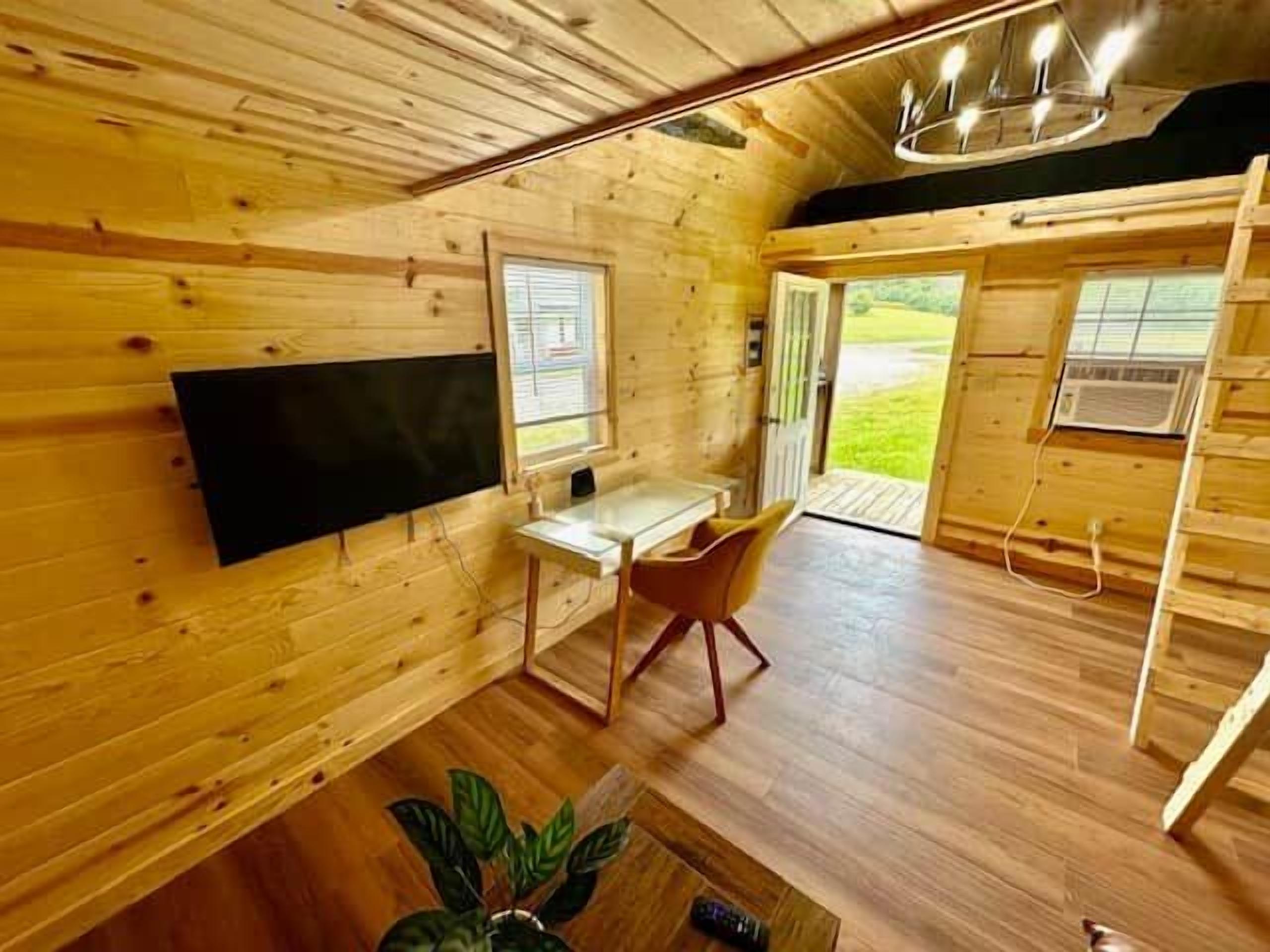 Un interior de madera con un escritorio, una silla, un televisor de pantalla plana y un ventanal grande.