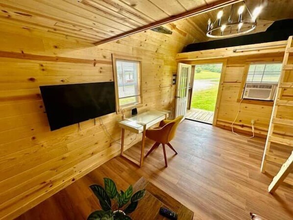 A wooden interior with a desk and chair, a flat-screen TV, and a large window. - Red Tiny Home in Copperhill TN (Copperhill)