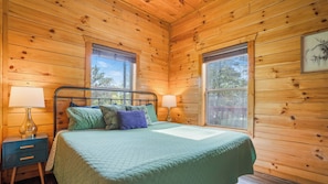 A wooden cabin bedroom with a bed, two bedside tables, and two windows. - Scenic Log Retreat • HotTub, Indoor Pool & Dogs OK (Sevierville)