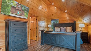 A log cabin bedroom with a bed, dresser, and a painting of a cabin. - Scenic Log Retreat • HotTub, Indoor Pool & Dogs OK (Sevierville)