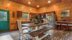 A wooden cabin kitchen with a dining table, chairs, a refrigerator, and a microwave.
