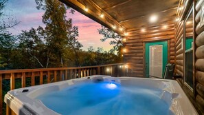 A hot tub on a wooden deck with a view of trees and a sunset. - Scenic Log Retreat • HotTub, Indoor Pool & Dogs OK (Sevierville)