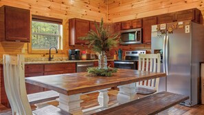 Cocina de cabaña de madera con una isla central, armarios de madera, un refrigerador de acero inoxidable y un microondas.